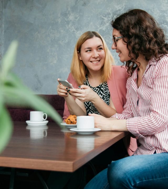 Two women enjoying a conversation over coffee and cupcakes in a cozy cafe setting.