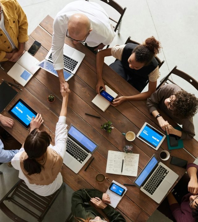 Top view of a diverse team collaborating in an office setting with laptops and tablets, promoting cooperation.