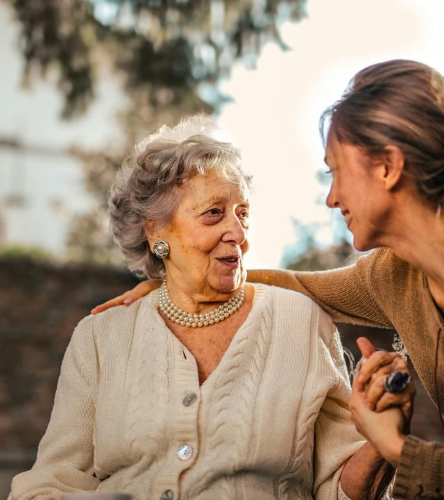 Elderly woman and adult daughter share a joyful, affectionate moment in a sunny garden.