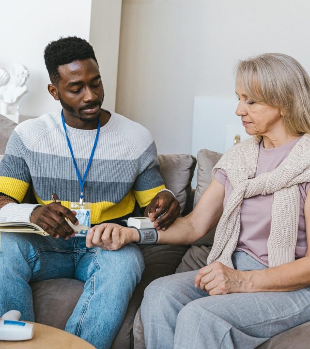 Volunteer checking elderly woman's blood pressure at home. Compassionate healthcare support.